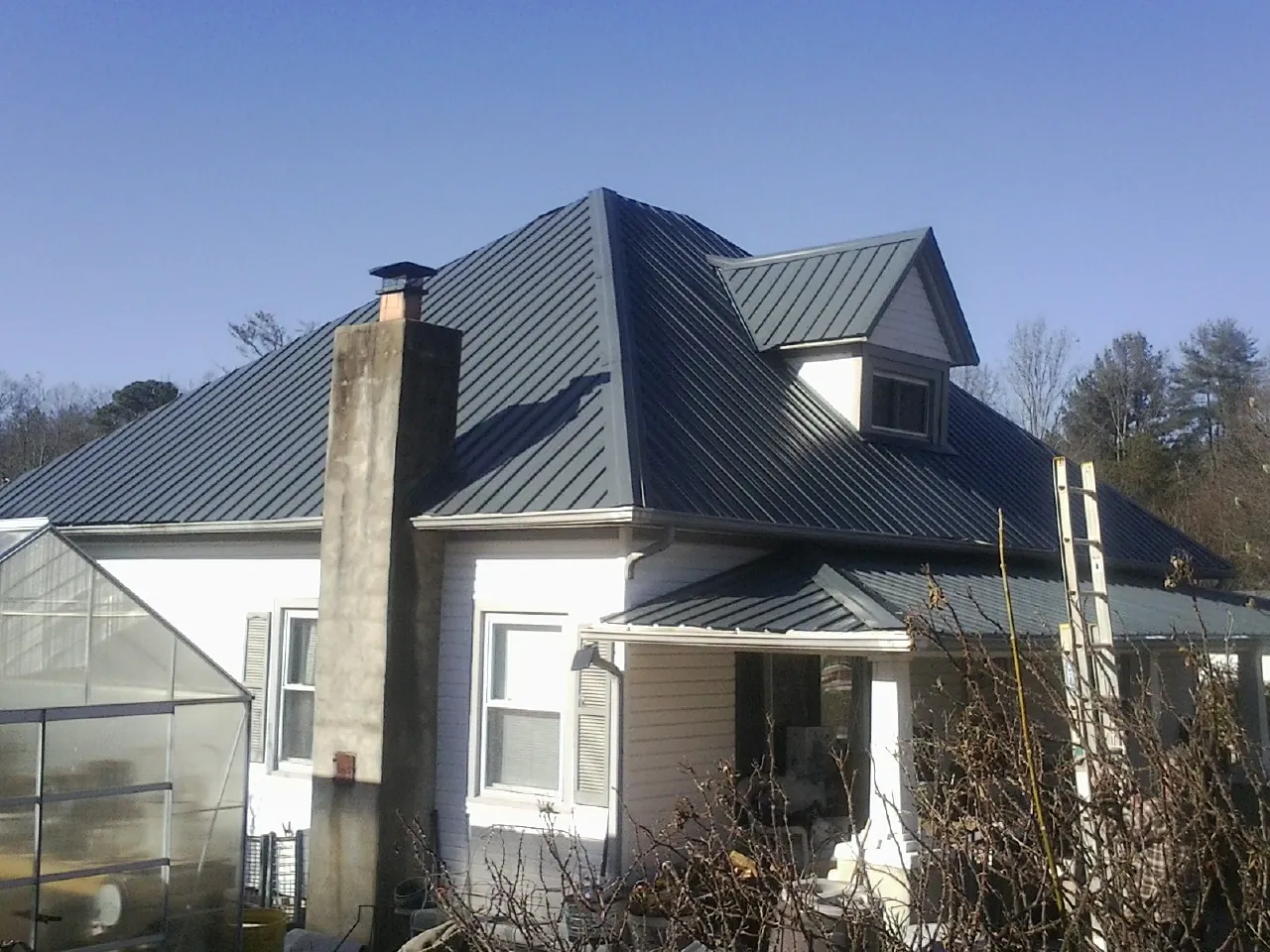 Dark blue standing seam metal roof on a white farmhouse with dormer — Slate & Tile Roof Repair by Roofing Brothers in Dickinson