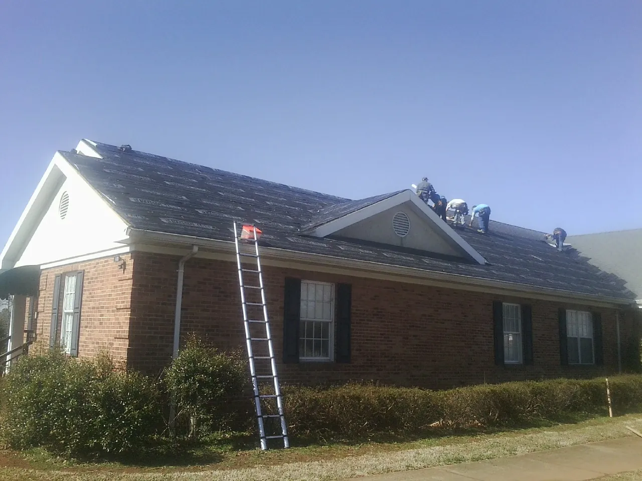 Crew tearing shingles off a brick ranch roof with a ladder set — Emergency Roof Repair work by our crew in Dickinson