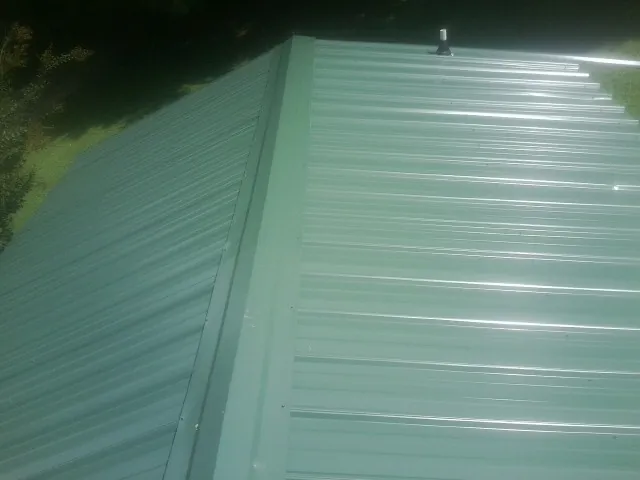 New green metal panels meeting at the ridge of a roof — Flat Roof Repair work by our crew in Dickinson