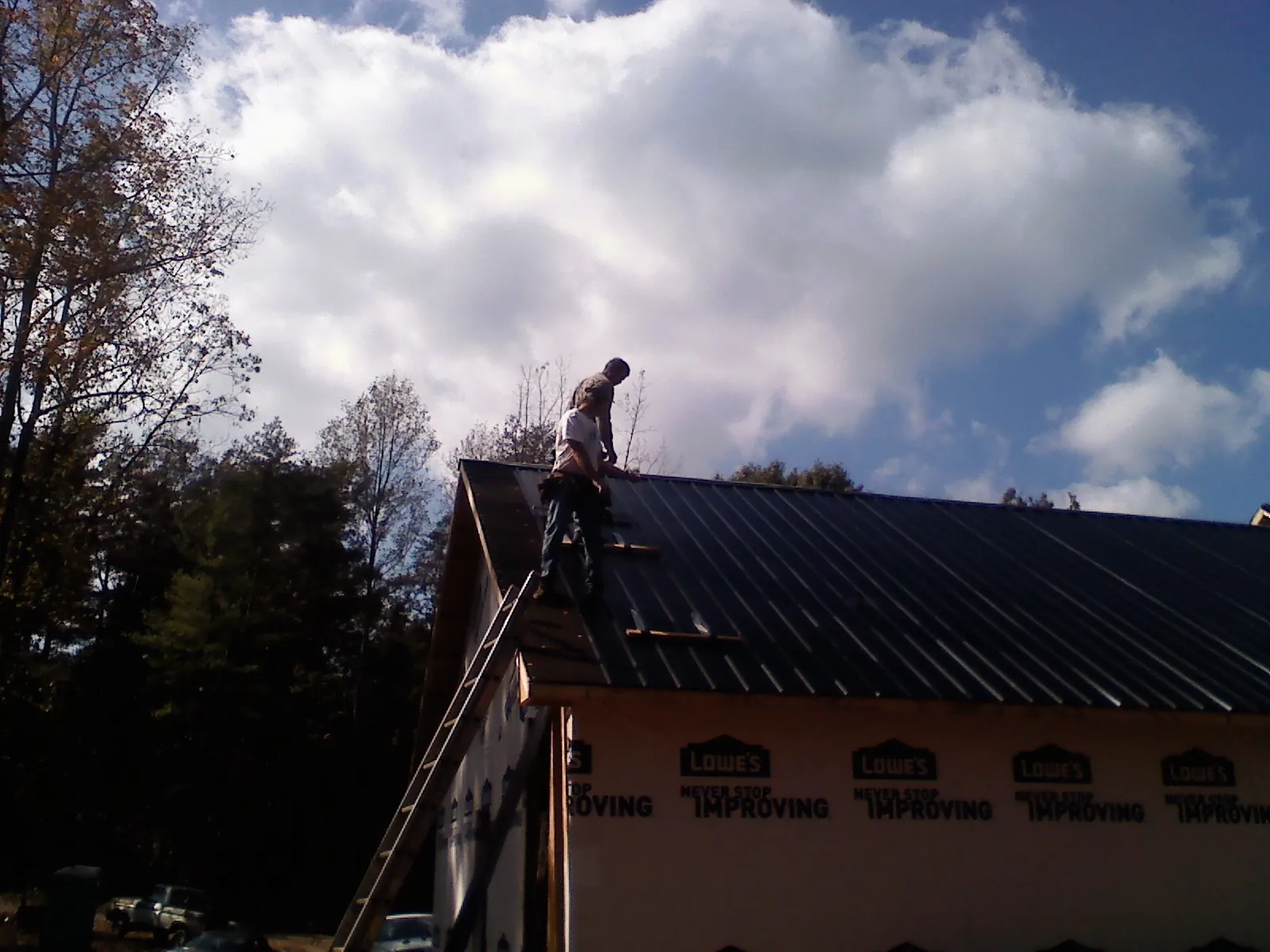Roofer fastening dark metal panels high against a cloudy sky, from a Roof Inspection job in Dickinson