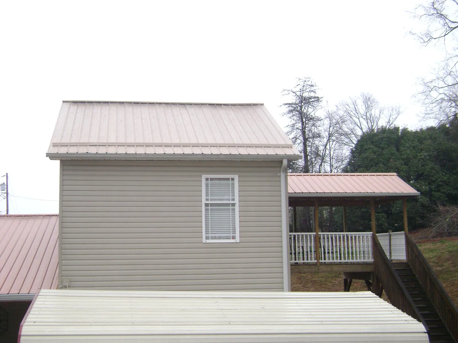 Tan metal roofs on a two story addition and attached porch, from a Roof Replacement job in Dickinson